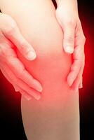 Woman touching her knee at pain point, with red spot on knee, isolated on black. Joint pain, Arthritis and tendon problems. Medical concept. Orthopedic problems. photo