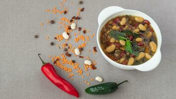 mexicano sopa de Siete tipos de frijoles, de cerca, en un gris lino antecedentes rodeado por rojo y verde pimientos y frijoles foto