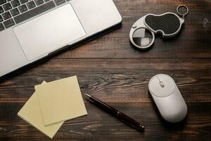 Laptop, opened magnifier, mouse, pen and paper for taking notes on the dark wooden table. Close up for your text photo