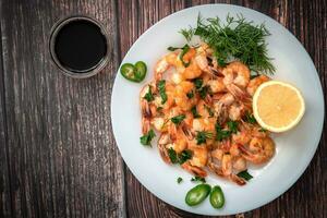 Fried shrimp in cream sauce with a plate closeup view from above on a table with lemon and dill, next to soy sauce photo