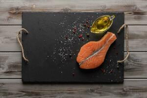 Raw salmon steak. On a dark board. Olive oil in an oil can. Healthy food. Top view. Wooden background photo