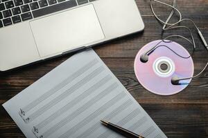 Laptop with headphones, CD and music paper with pen on wooden background. Copy space for your text. Top view. Outdated and modern storage photo