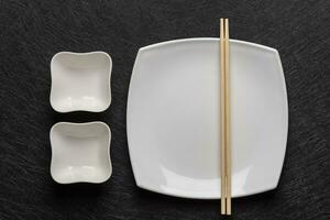 vacío blanco plato con palillos y dos salsa barcos en un oscuro antecedentes. japonés comida estilo. parte superior ver foto
