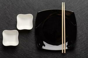 Empty square black plate with chopsticks and two white gravy boats on a dark background. Japanese food style. Top view photo