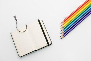 Clean notepad and rainbow color pencils in the shape of an arrow on a white background top view photo