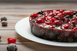 Pie with berries closeup, raspberry, currant, strawberry on a white plate on a wooden background, near red currant and cherry photo