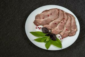 Baked meat cut into pieces on a white plate with basil and red pepper grains closeup top view on a black background photo