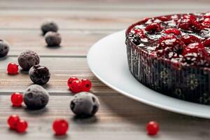 Pie with berries, raspberry, currant, strawberry on a white plate on a wooden background, near red currant and cherry photo