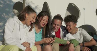 Group of happy teenage friends looking the phone and laughing in the city street. video