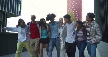 Multiethnic group of young happy friends walking and jumping down the street holding each other affectionately. video