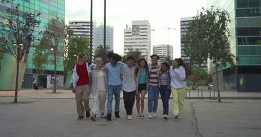 multiétnico grupo de joven contento amigos saltando a el mismo hora caminando abajo el calle participación cada otro afectuosamente. video