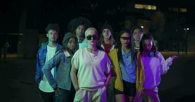 Multiethnic group of young people posing looking at camera in the city at night with colored neon lights. video