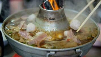 cerca arriba de hombre utilizar madera palillos poner albóndigas son mezclado juntos Cerdo en caliente sopa en maceta. cocido a fuego lento carne de vaca con menudencias y albóndiga sopa en caliente maceta video