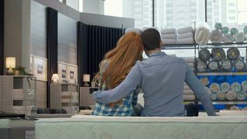 Rear view shot of a couple hugging, sitting on a new bed at furniture store video