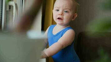 luidruchtig kleuter jongen. echt van streek baby staand in de buurt venster Bij huis. video