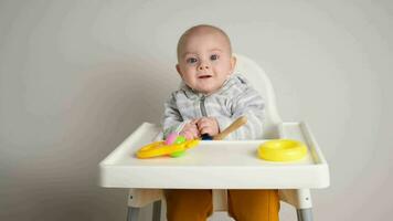 schattig zuigeling jongen zittend Aan baby hoog stoel met plastic ontwikkelen speelgoed. video