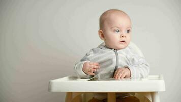 bebis sitter på bebis hög stol. spädbarn vänder genom sidor och utseende på bok. video
