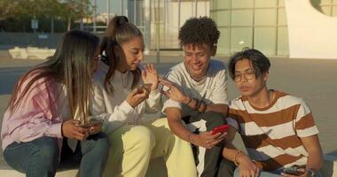 groupe de multiculturel content adolescent copains à la recherche le téléphone et en riant dans une banc dans le ville rue. video