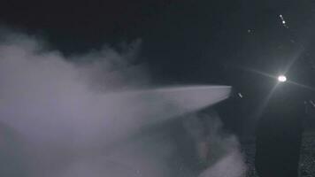 Unrecognizable fireman silhouette combating a fire of a burning car accident at night. video