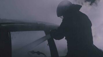 Unrecognizable fireman silhouette combating a fire of a burning car accident at night. video