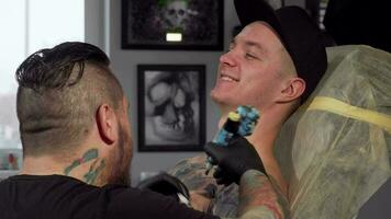 Cheerful young man smiling to the camera, while getting tattooed video