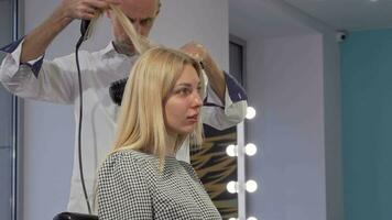 Lovely young woman smiling, while getting her hair styled by hairdresser video