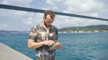 Young man using tablet while walking. Working by the sea. video