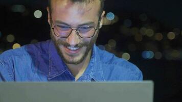 Happy young man working on his laptop by the sea at night. video