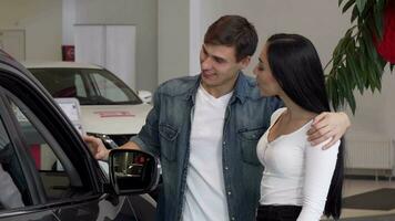 joven Pareja elegir nuevo coche a el concesión, mirando dentro el automóvil video