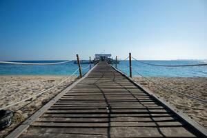 Long wooden pier bridge extents from beach to turquoise wave sea. Deep Blue cloudy sky after the big storm. Expectation to success dreams,Travel and summer Vacation, Freedom and youth Concept. photo