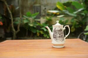 ceramic teapot on wooden table with garden background photo