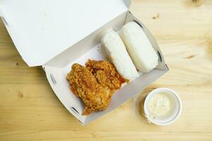 Fried chicken with boxed rice and carbonara sauce in a box on a wooden background photo