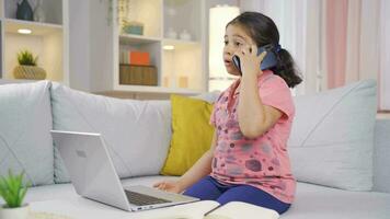 Girl child using laptop nervously talking on the phone. video