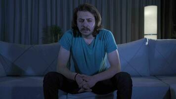 Depressed and worried young man sitting alone on sofa at home. video