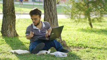 Université nain étudiant séance dans le parc et Faire recherche. video