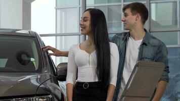 Happy young couple buying new automobile at the dealership, reading info paper video