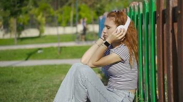 jovem mulher sentado em a terra ao ar livre escuta para triste música e é infeliz. video