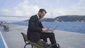 Businessman sitting on the bench works from his laptop. Slow motion. video