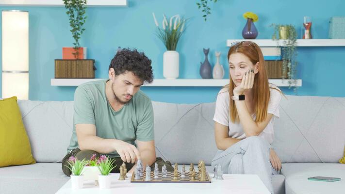 young couple playing chess while sitting at table at home - Unpacked