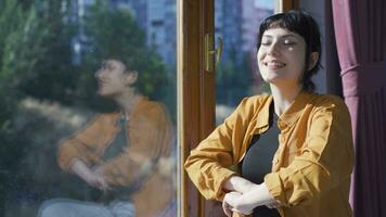 Happy young woman looks out the window and takes a deep breath. video