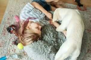 Little girl playing with a golden retriever puppy at home. photo