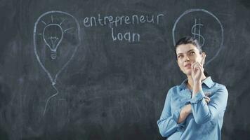 Woman writing entrepreneur loan on blackboard looks up with happy expression. video