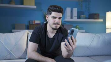 Young man looking at his smartphone at home feeling emotional and upset. video