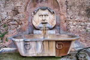 a fountain with a face on it in front of a brick wall photo