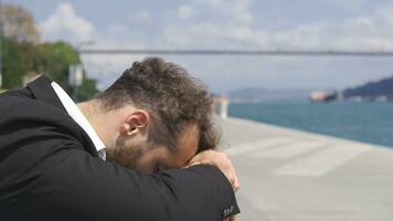 Sad businessman by the sea. He puts his head in front of him. video