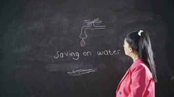 Woman writing water conservation on blackboard looks happily at camera. video