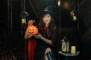 Asian girl in witch costume holding jack o lantern for halloween party trick or treat concept with dark black background photo