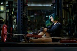 Asian woman is facing overtraining syndrome after weight training workout inside gym with dark background for exercising and fitness concept photo