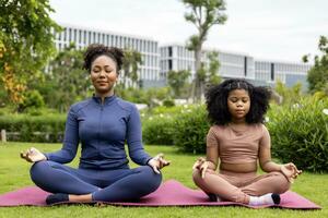 African American woman and her daughter in yoga suit are relaxingly practicing meditation exercise in the park to attain happiness from inner peace wisdom for healthy mind and soul concept photo