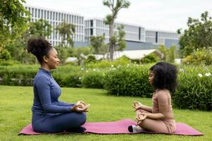 African American woman and her daughter in yoga suit are relaxingly practicing meditation exercise in the park to attain happiness from inner peace wisdom for healthy mind and soul concept photo